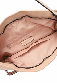Beige leren handtas interieur met een zachte stoffen voering, bevat een ritsvak en een label. Donkere ritsafsluiting aan de bovenkant.