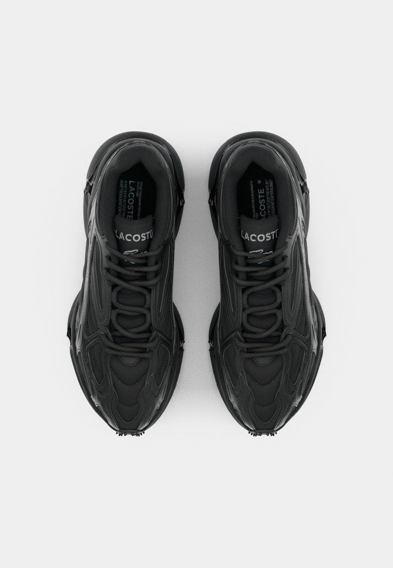 Black athletic shoes with a textured design, featuring a rounded toe, laces, and the Lacoste logo on the tongue and side.