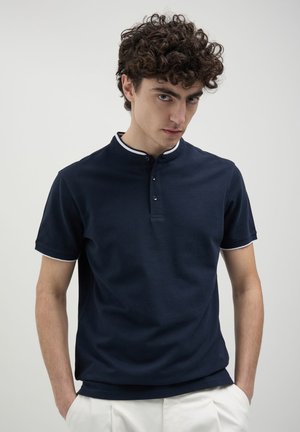 Polo shirt marine avec un col à boutons, bordé de blanc au niveau du col et des manches. Fabriqué en tissu doux, à manches courtes, coupe classique.
