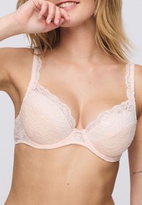 Lacey pink bra with underwire, featuring floral patterns, adjustable straps, and a center bow detail for added embellishment.