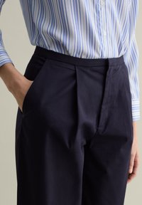Pantalones de vestir azul marino con textura suave y bolsillos laterales, combinados con una camisa de botones a rayas azul claro.