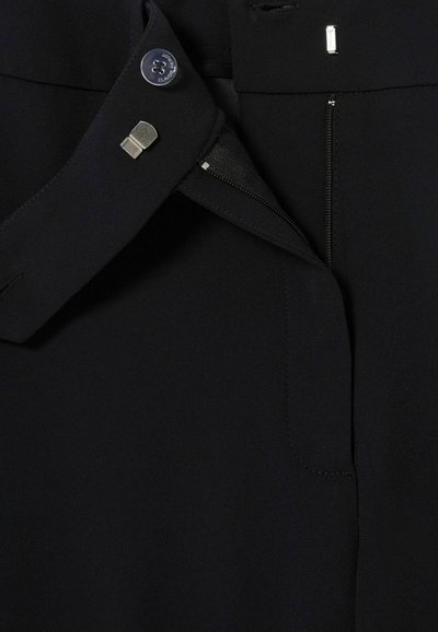 Tejido negro con una cinturilla plana y cierre de botón, detalle de cremallera y costuras sutiles. Textura suave sin patrones visibles.