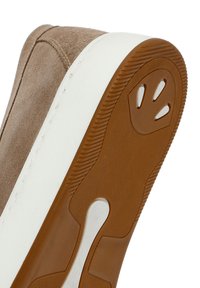 Bruine suède sneaker met een gestructureerde, gumrubberen zool met een witte rand. De zool heeft opvallende groeven en een pootafdrukdetail.