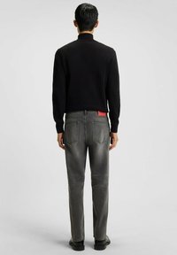 Zwarte trui en grijze denim jeans. De trui heeft een hoge kraag, terwijl de jeans een rood merklabel en een vervaagde afwerking hebben.