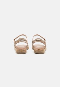 Tan sandals with braided straps, adjustable ankle buckle, and a textured espadrille sole. Open-back design for breathability.