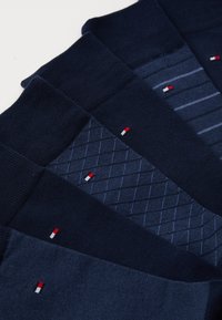 Fire par navy sokker med forskjellige teksturer og mønstre, inkludert ensfargede, stripete og diamantmønstre, hver med en liten logo.