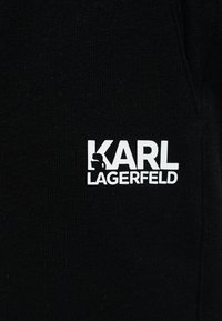 Μαύρο ύφασμα με λευκό λογότυπο κειμένου "KARL LAGERFELD" που απεικονίζει τη σιλουέτα ενός άνδρα που στηρίζεται στο γράμμα "K".