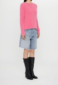 Różowy puszysty sweter, dżinsowe szorty z postrzępionym dołem i wysokie czarne botki na obcasie. Sweter ma okrągły dekolt i długie rękawy.