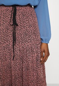 Jupe rose avec un imprimé léopard noir, présentant une texture plissée et un cordon de serrage noir à la taille ; associée à un haut bleu à manches longues.