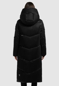 Juodas ilgas pūkinis paltas su dideliu gobtuvu, pasižymintis zigzaginio siuvinėjimo raštu ir blizgiu paviršiumi. Mažas logotipo detalė šalia apatinės krašto.