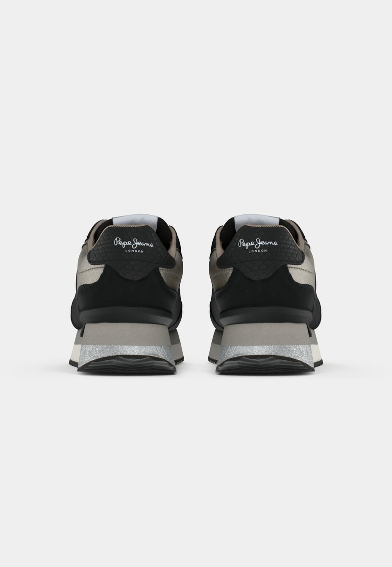 Schwarze und beige Sneakers mit einer strukturierten Oberfläche, präsentiert mit einem silbernen Akzent an der Sohle, einem Logo auf der Rückseite und einer gepolsterten Ferse.