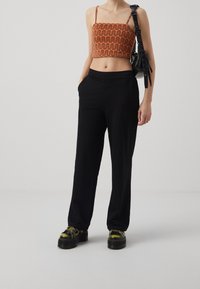 Černé široké kalhoty v kombinaci s cropped topem s vlnitým oranžovým vzorem. Modelka má na sobě robustní černé platformové boty.