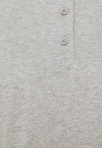 Tissu gris clair avec deux boutons blancs cousus verticalement près d'un bord cousu, les boutons sont embossés du texte "NIKE".