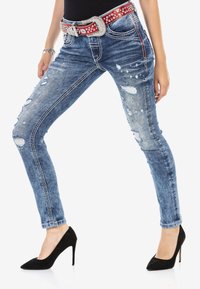 Verwaschene blaue Jeans im Slim-Fit, mit einem mit Strass verzierten roten Gürtel und schwarzen High Heels.