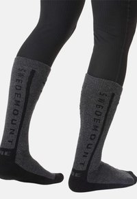 Kniestrümpfe in Dunkelgrau mit gerippter Struktur, mit auffälligen schwarzen Buchstaben entlang der Seiten und kontrastierenden schwarzen Akzenten an Zehen und Ferse.