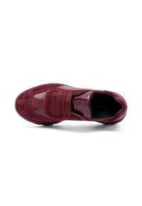 Chaussure de sport bordeaux mettant en avant un mélange de daim et de matériaux brillants, des sangles élastiques, un bout rond et des accents texturés sur les côtés.