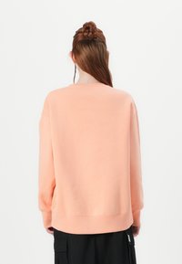 Sweatshirt rosa com um corte descontraído, gola redonda canelada e mangas longas. Textura suave e bainha reta, combinado com calças cargo pretas.