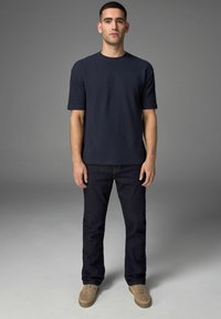Navy Crewneck-T-Shirt mit kurzen Ärmeln, kombiniert mit dunkelblauen Jeans und hellbraunen Schnürschuhen, mit einem lässigen Schnitt.
