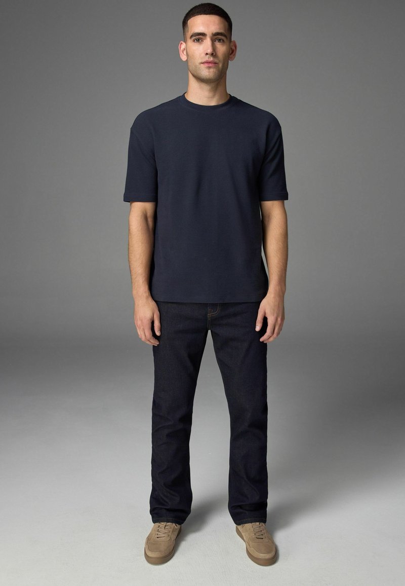 Navy Crewneck-T-Shirt mit kurzen Ärmeln, kombiniert mit dunkelblauen Jeans und hellbraunen Schnürschuhen, mit einem lässigen Schnitt.