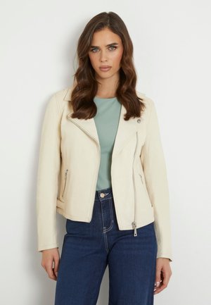 Giacca da moto in pelle color crema con zip, vestibilità slim e collare a revers, abbinata a una maglia turchese chiaro e jeans in denim scuri.
