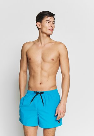 Bright blue swim shorts with a drawstring waist, side pockets, and a small black logo patch. The material appears lightweight and smooth.