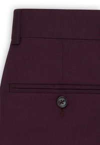 Zbliżenie na ciemno bordowe teksturowane spodnie wizytowe, pokazujące tylną kieszeń z czarnym guzikiem oraz szlufkę na pasek przy talii.