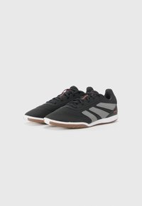 Black athletic shoes with mesh upper, gray side stripes, red accents, and rubber sole. Designed for flexibility and support in sports activities.