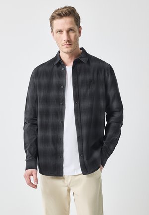 Zwarte overhemden met een geruit patroon, voorzien van lange mouwen en een eenvoudige kraag, gelaagd over een wit T-shirt.