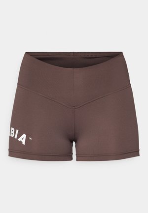 Brūni sporta šorti ar augstu jostasvietu, elastīgu audumu un baltu logo detaļu kreisajā pusē. Gluda tekstūra un pieguļošs dizains.