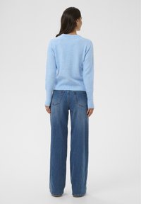 Svijetloplava džemperica od mekog materijala, upotpunjena trapericama s visokim strukom i širokim nogavicama. Ima okrugli izrez i rebraste manžete.