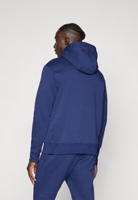 Mørkeblå hoodie lavet af blødt materiale, med en klassisk snørehætte, ribbede manchetter og en lige kant. Enkel design med en glat overflade.