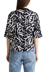 T-shirt à manches courtes en noir avec un motif abstrait blanc, offrant une coupe décontractée et un tissu lisse. Associé à un jean en denim bleu clair.