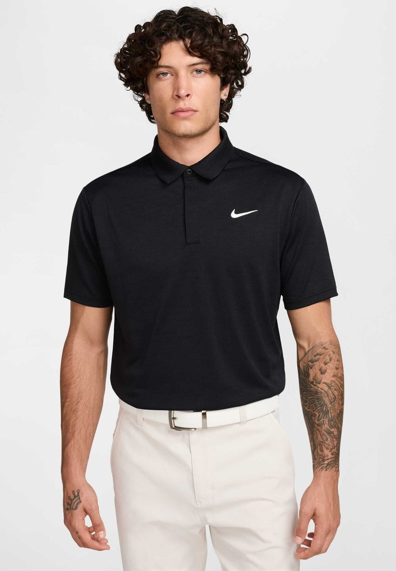 Melns polo krekls ar klasisku apkakli, īsām piedurknēm, Nike logo baltā krāsā kreisajā krūtī; apvienots ar baltām biksēm un sudraba jostu.
