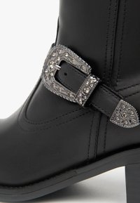Stivale alla caviglia in pelle nera con fibbia decorativa in argento con strass, dettagli cuciti e tacco a blocco.
