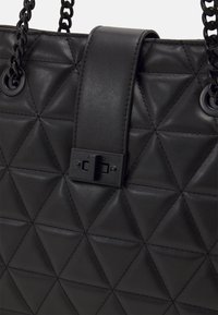 Czarna pikowana torebka ze skóry z trójkątnym wzorem, wyposażona w płaski pasek i metalowe zapięcie. Uchwyty łańcuchowe w kolorze czarnym.