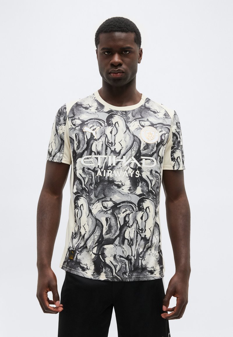 Man draagt een voetbalshirt met korte mouwen met zwart-witte paardontwerpen, het Etihad Airways-logo en het Puma-logo op een lichte achtergrond.