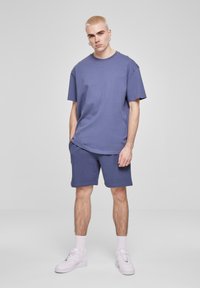 Tricou din bumbac violet, lejere și pantaloni scurți asortați. Textură netedă, de tip crew, și mâneci relaxate. Adidași albi completează ținuta.