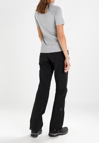 Chemise grise à manches courtes assortie à un pantalon noir. La chemise a une texture lisse, tandis que le pantalon présente une coupe ample avec des détails de fermeture au niveau des chevilles.