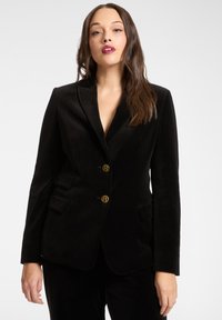 Blazer in velluto nero con vestibilità sartoriale, bottoni dorati, rever a lancia e tasche laterali. Tessuto liscio e silhouette elegante.