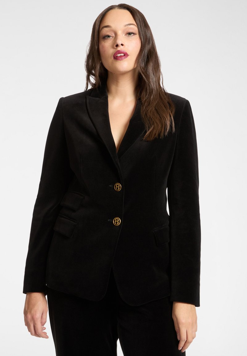 Blazer in velluto nero con vestibilità sartoriale, bottoni dorati, rever a lancia e tasche laterali. Tessuto liscio e silhouette elegante.