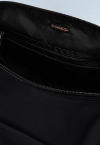 Borsa di tessuto nera con un esterno opaco, cuciture dettagliate, chiusura con zip e un'etichetta cucita all'interno. L'interno presenta una fodera liscia.