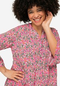 Robe fleurie avec une base rose et des motifs floraux multicolores, fermée par des boutons, avec une taille froncée. Manches longues avec une coupe décontractée.
