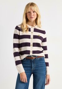 Stribet cardigan i creme og mørk lilla, lavet af blødt stof. Har rund halsudskæring, knaplukning foran og en lille hjerteformet detalje.