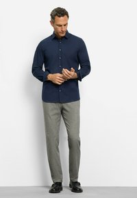 Marineblaues Langarmhemd mit Knopfverschluss, getragen mit grauen strukturierten Hosen und schwarzen Schuhen. Das Hemd hat einen spitzen Kragen und enganliegende Ärmel.