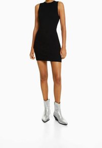 Robe mini sans manches noire à côtes avec une silhouette ajustée, associée à des bottes à chevilles argentées métalliques avec un bout pointu et un talon carré.