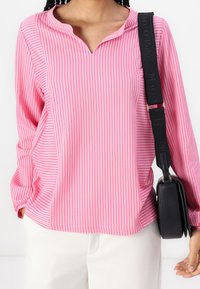 Vaaleanpunaisessa raidallisessa paitapuserossa on V-pääntie ja pitkät hihat. Paita on yhdistetty kermaisenvärisiin housuihin ja pieneen mustaan olkalaukkuun.