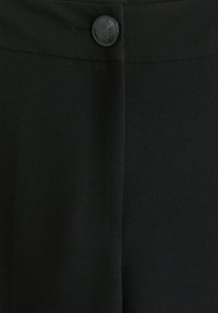 Pantalons en tissu noir avec une texture lisse, présentant un bouton visible et un détail de couture sur le côté. La conception est ajustée avec une finition soignée.