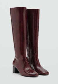 Burgundy, polvenpituiseen saapikkaat kiiltävästä materiaalista, jossa on pystysuorat tekstuuriviivat, teräväkärkiset ja loiva korko. Vetoketjusuljenta sivussa.