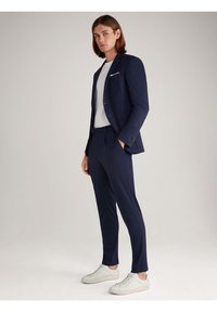 Marineblauer Anzug mit tailliertem Schnitt, bestehend aus einem Blazer und passenden Hosen, kombiniert mit einem weißen T-Shirt und weißen Sneakern.