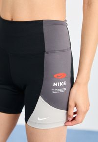 Shorts Nike negri și gri cu talie înaltă. Au un logo reflectorizant și text alb, cu un finisaj dintr-un material neted și elastic.